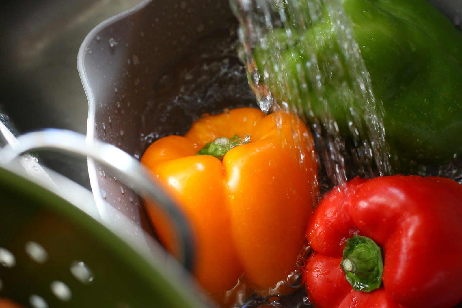 Bell peppers being rinsed under running water in a colander